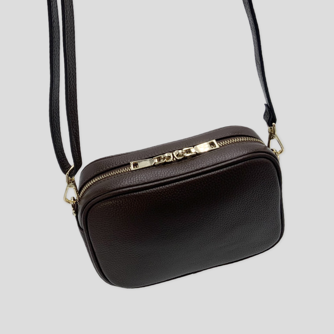 Classic elegance with practicality and versatility in mind. TIKORI classic dark brown by TIKORI london. Genuine leather crossbody bag. Back profile of the bag showing in the picture in hanging motion . Golden tone hardware and leather strap detail shows in white background.
