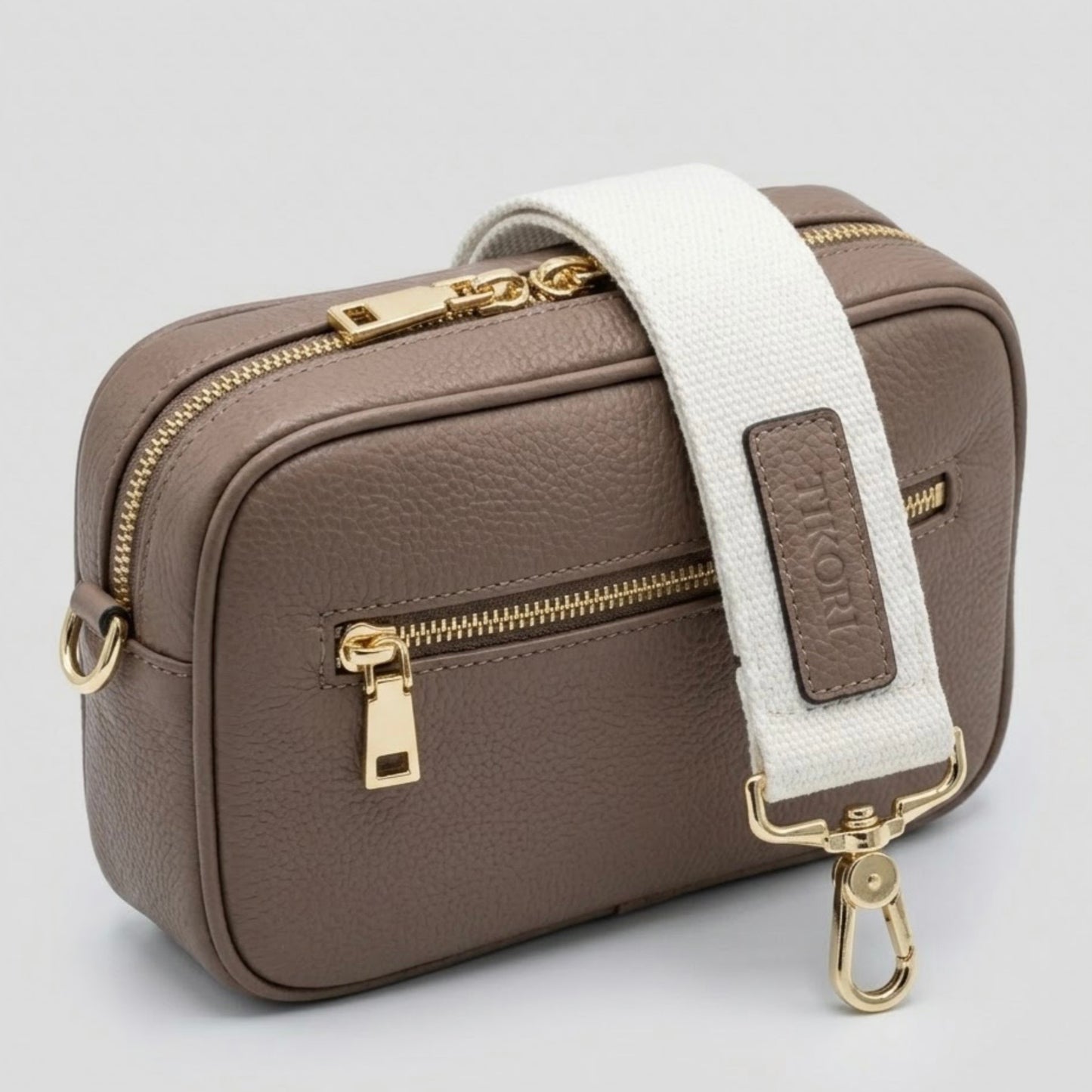 TIKORI classic mink by TIKORI London. Classic elegance with practicality and versatility in mind. Mink leather cross body bag shows in the picture with golden tone hardware and signature TIKORI canvas strap over the bag. . Front profile includes the gold zipper pocket. Bag display in a white background.