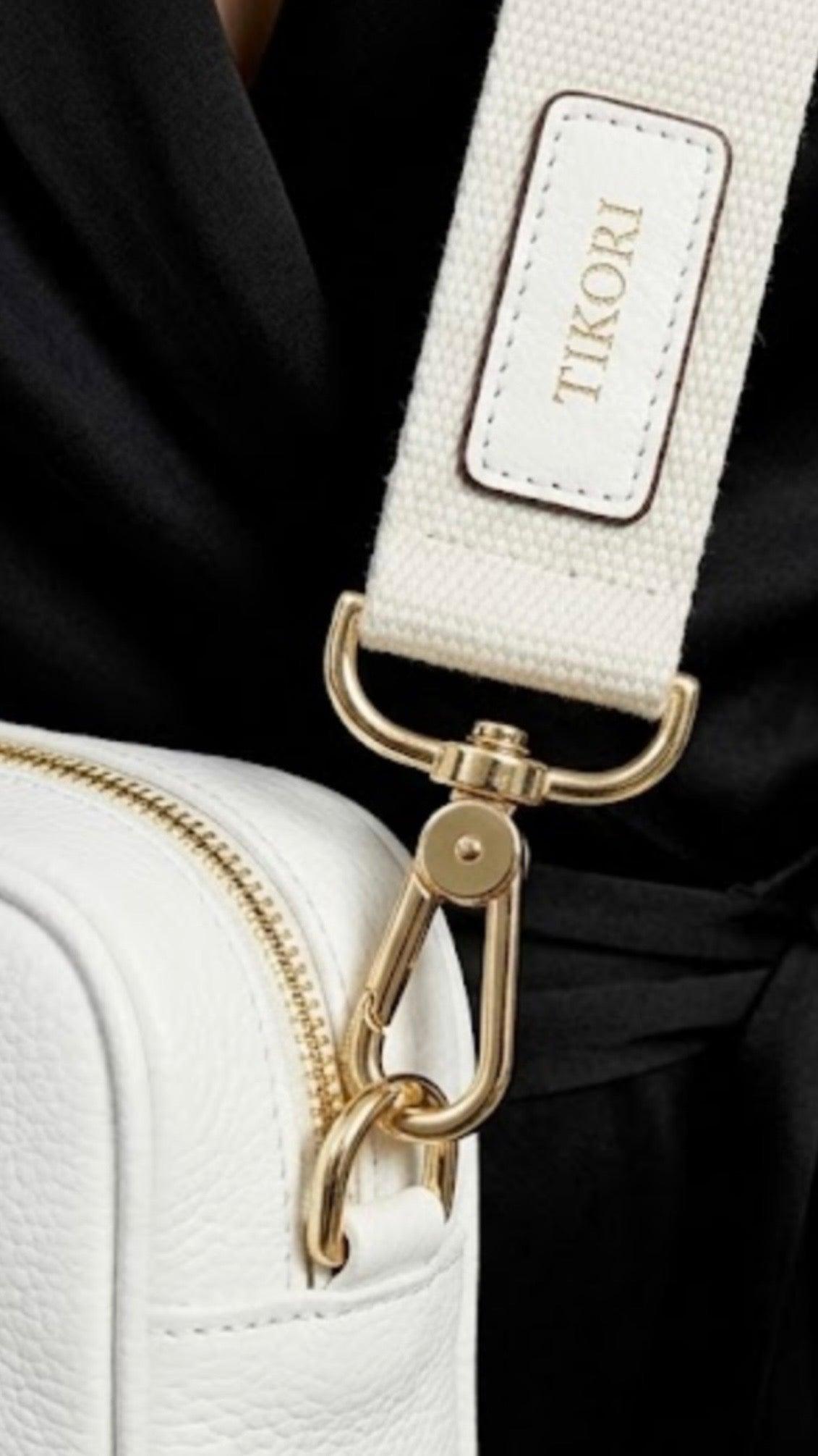 Classic pebbled leather cross body bag - White - TIKORI LONDON. Model in black silk cloths wears the crossbody. Close up detail of the golden tone hardware and canvas strap with TIKORI logo shows in the picture.