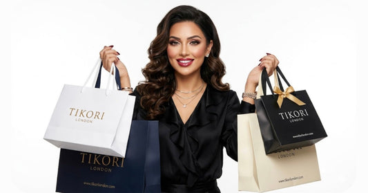TIKORI LONDON. Beautiful female model wearing black top holding few bags up highlighted TIKORI LONDON and smiling. Fully white background.