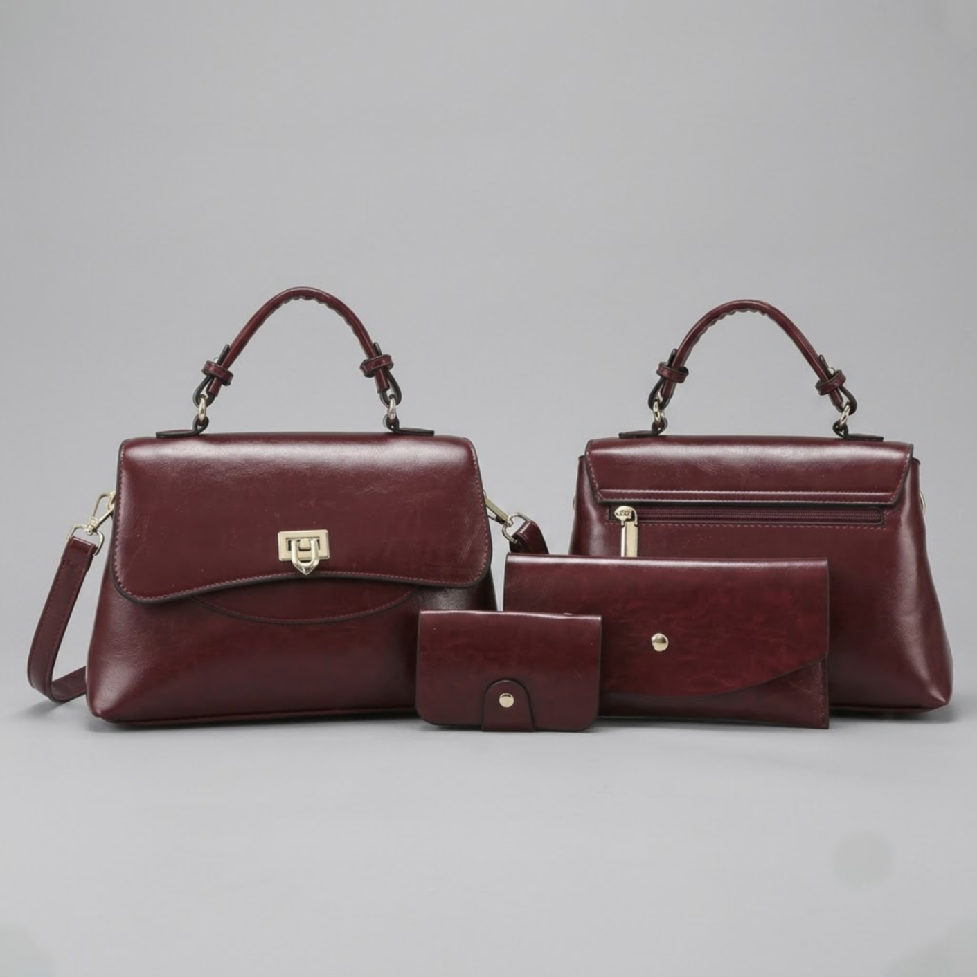 Heritage flap bag maroon by TIKORI LONDON. Defined by a unique braided leather handle that adds a touch of luxury. Features a beautiful, sweeping front flap secured by a polished, shield shaped gold clasp. One bag facing front and the other facing back showing both profiles. Card holder and wallet also sit next to bags. Display on the floor.