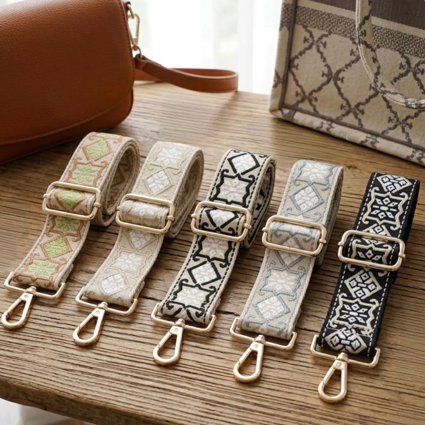 Woven geometric patterned Cross Body Bag Straps By TIKORI london. Soft geometric patterns with sleek design with golden tone hardware. For instance style upgrade. 5 straps displays on a wooden table next to two beautiful handbags, home background.