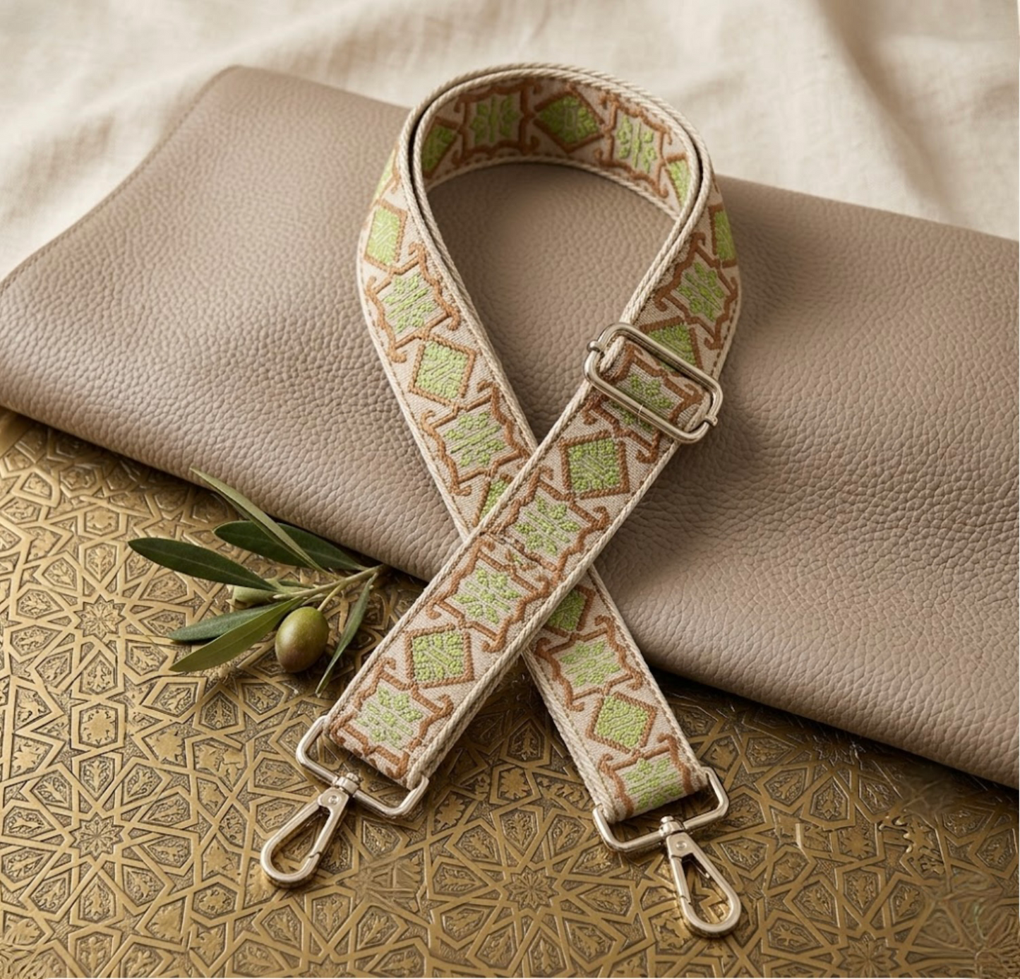 Woven Cross Body Bag Strap - Sage Verde By TIKORI london. Soft geometric patterns with sleek design with golden tone hardware. For instance style upgrade.  Display on a metal gold table with taupe leather piece. One olive in a small branch next to it.