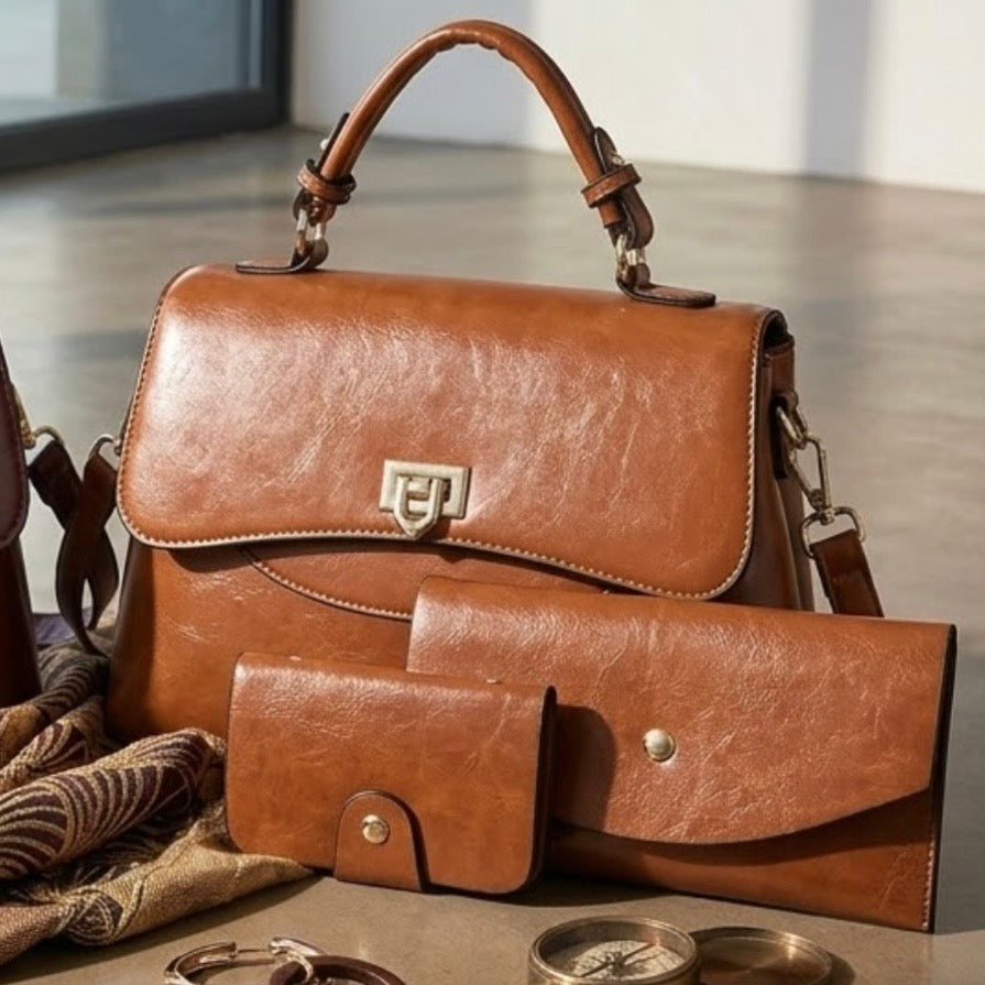 Heritage Flap Bag - Tan  By TIKORI London. Features a beautiful, sweeping front flap secured by a polished, shield shaped gold clasp. Top handle and long strap included. Front of the bag showing on the picture with matching wallet and cardholder on the floor, next to a scarf and some jewellery. Golden hardware and curved top handle and golden front lock visible.