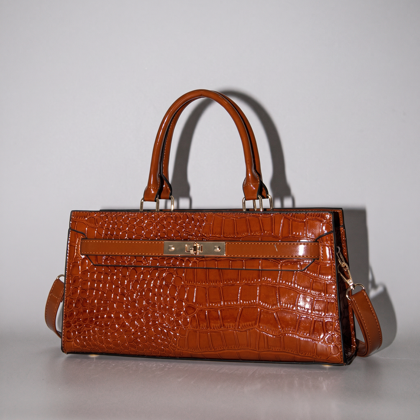 Gilded Croc Baguette - Cognac By TIKORI London. Front golden lock detail showing on the picture. Top handles detail with Golden tone hardware. With Shining light reflection detail on the picture.