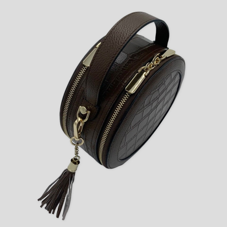 Cleopatra by Tikori London. Dark brown  leather circle crossbody bag with dual zip fastening, featuring a sleek finished leather design. Front profile shows in white background. 