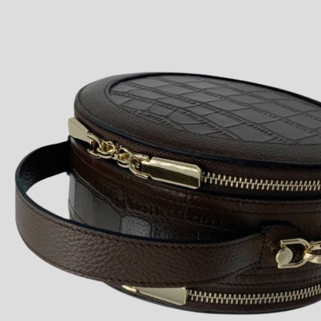 Cleopatra by TIKORI london. Dark brown leather circle crossbody bag with dual zip fastening. featuring a sleek finished leather design. Close up details of the handle and zipper showing in the picture.