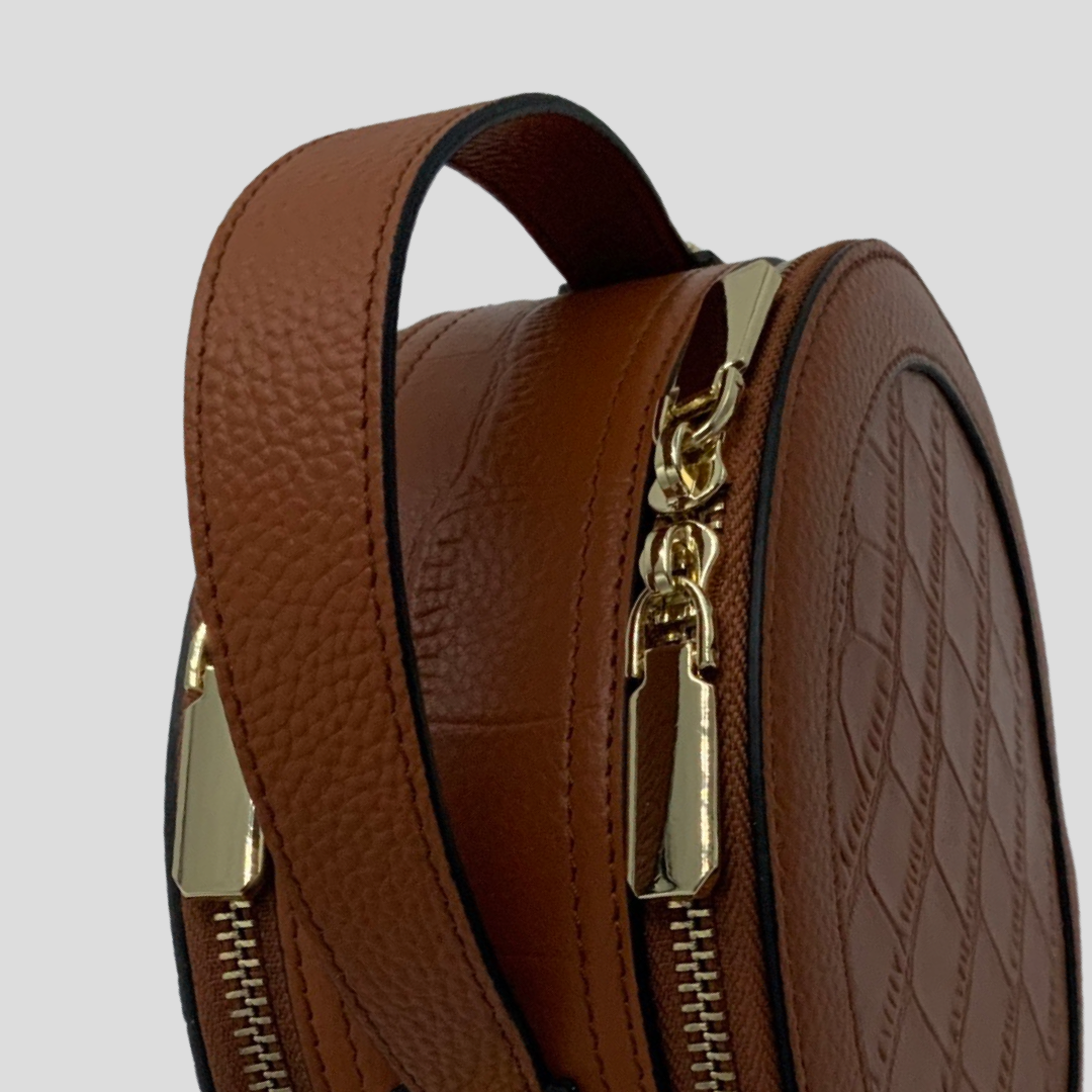Cleopatra by TIKORI London. warm tan leather circle crossbody bag with dual zip fastening and finished leather design. Close up Top handle shows on the picture.