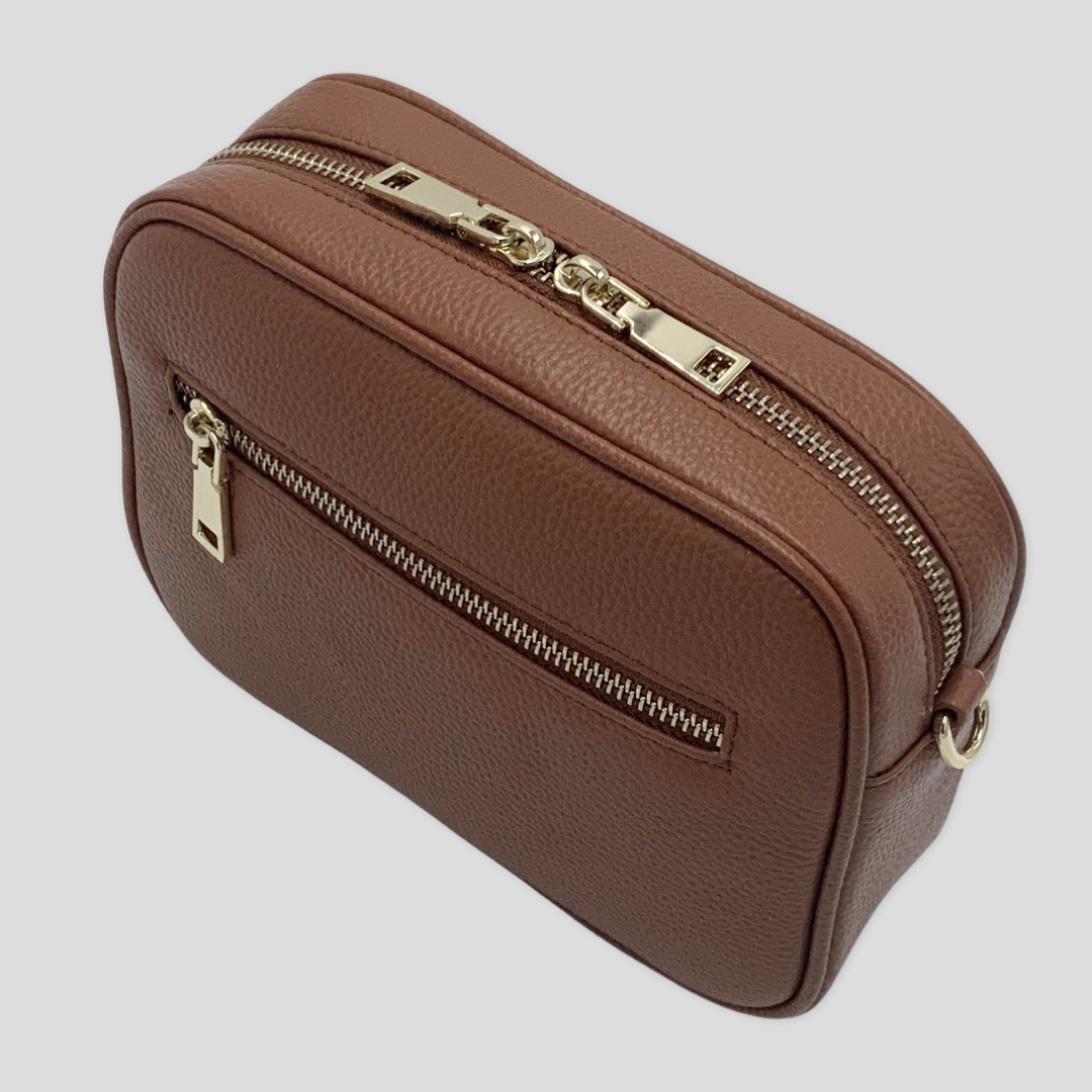 Classic elegance. TIKORI London classic pebbled leather crossbody bag in warm tan with adjustable strap and sleek design. Front profile of the bag showing in the picture. Close up detail of the golden hardware shows in white background 