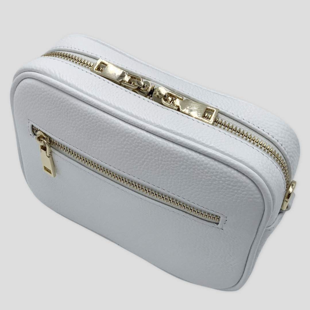 Classic elegance. Tikori Classic White by TIKORI london.  Genuine pebbled leather cross body bag. Front  profile of the bag showing the zipper details, gold hardware and front pocket. 