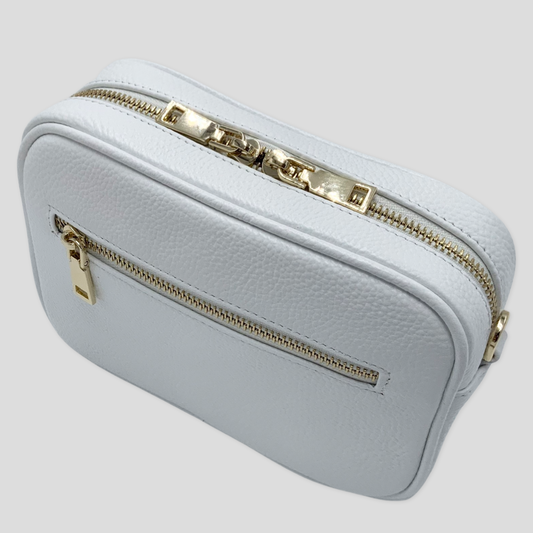 Classic elegance. Tikori Classic White by TIKORI london.  Genuine pebbled leather cross body bag. Front  profile of the bag showing the zipper details, gold hardware and front pocket. 