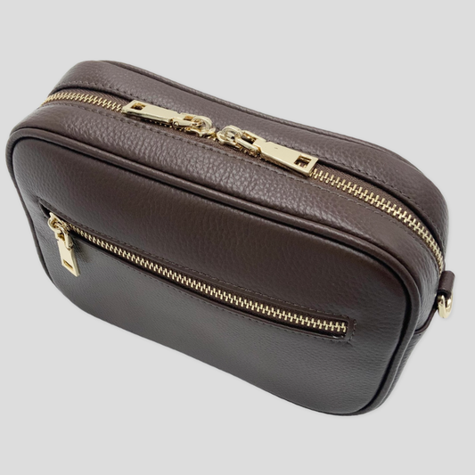 Classic elegance with practicality and versatility in mind. TIKORI classic dark brown by TIKORI london. Genuine leather crossbody bag. Front profile of the bag showing in the picture. Golden tone hardware and front pocket zipper detail shows in white background. 