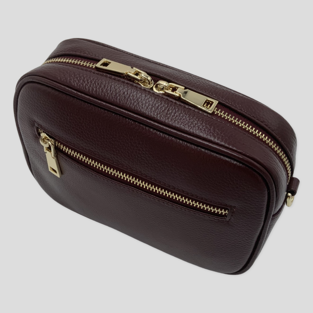 Classic elegance with practicality and versatility in mind. TIKORI classic maroon by TIKORI london. Genuine Leather crossbody bag. Front profile of the bag showing with golden tone hardware. Front zipper details and front pocket shows in white background. 