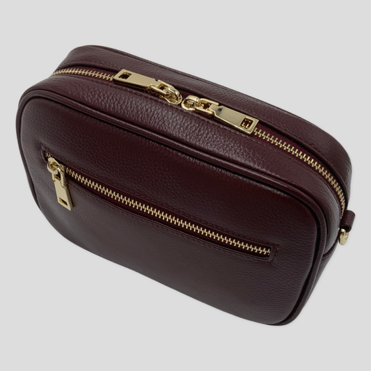 Classic elegance with practicality and versatility in mind. TIKORI classic maroon by TIKORI london. Genuine Leather crossbody bag. Front profile of the bag showing with golden tone hardware. Front zipper details and front pocket shows in white background. 