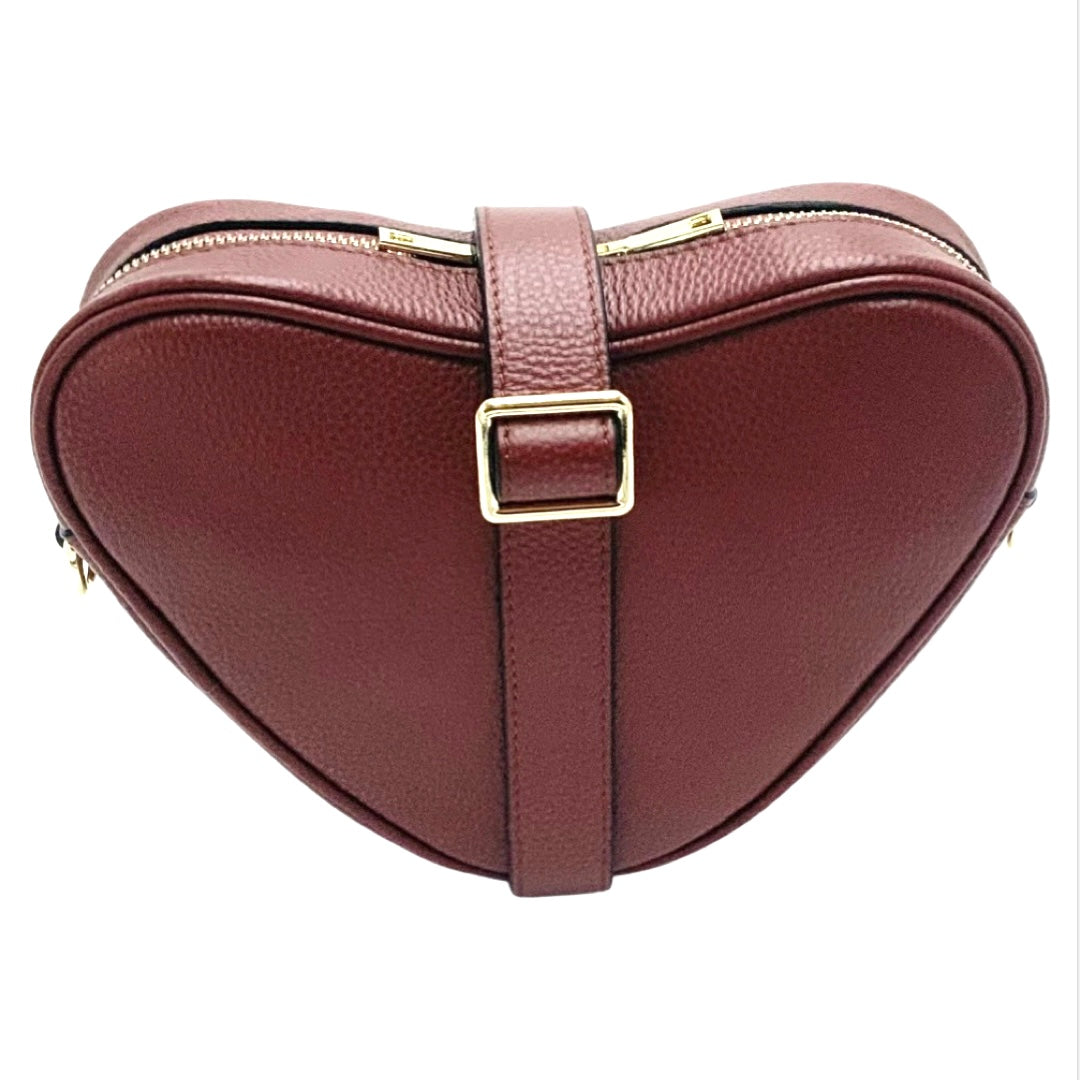 Red brown heart-shaped leather crossbody bag by Tikori London with adjustable strap and gold-tone hardware. Front profile of the bag showing in the picture. Strap is wrapped around the bag showing the golden tone buckle in fully white  background.