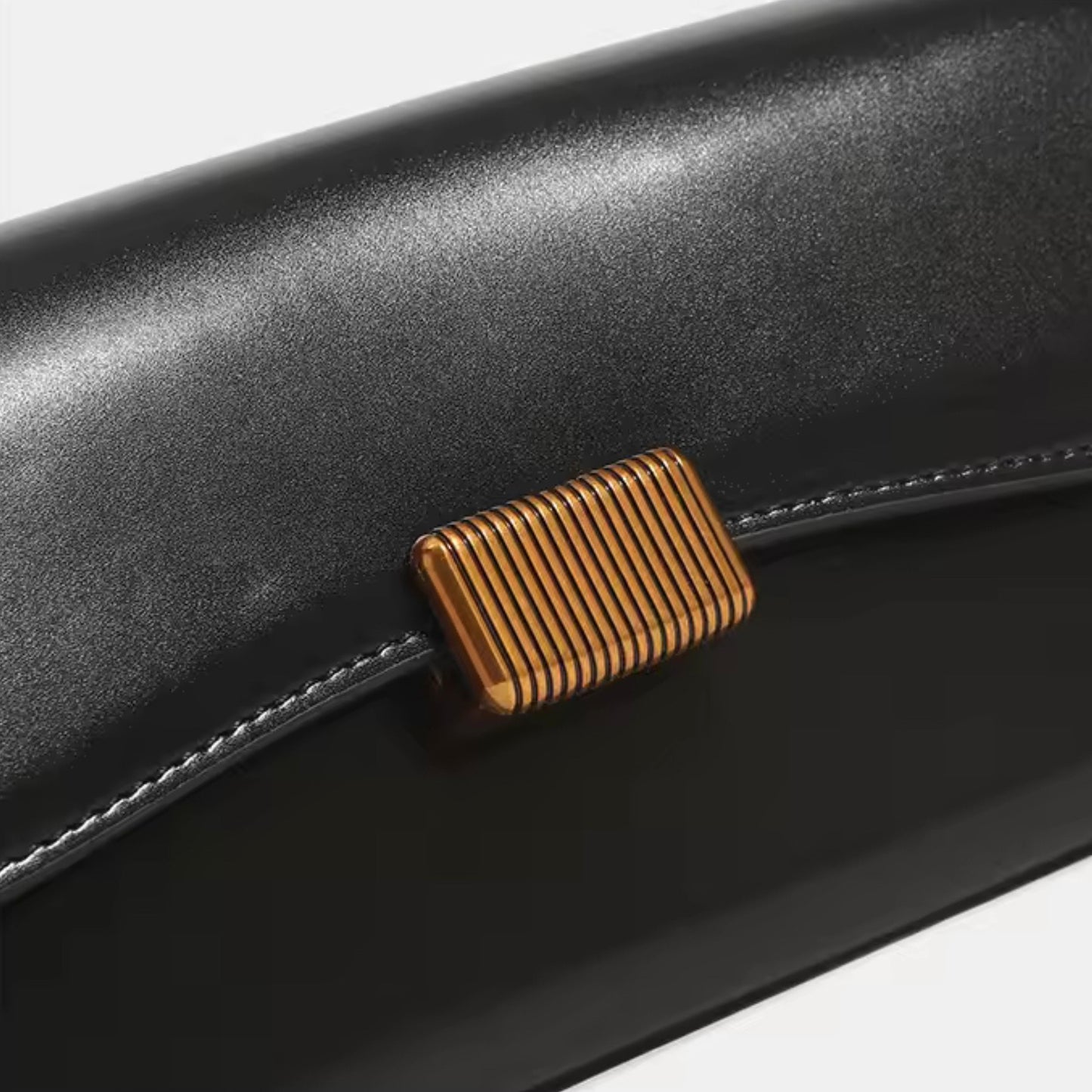 Crimson Muse Shoulder Bag - Black by TIKORI LONDON. Features a structured, elongated "baguette" body with clean, sharp lines and a narrow profile designed to sit snugly under the arm. Picture shows the front clasp details of the bag. 