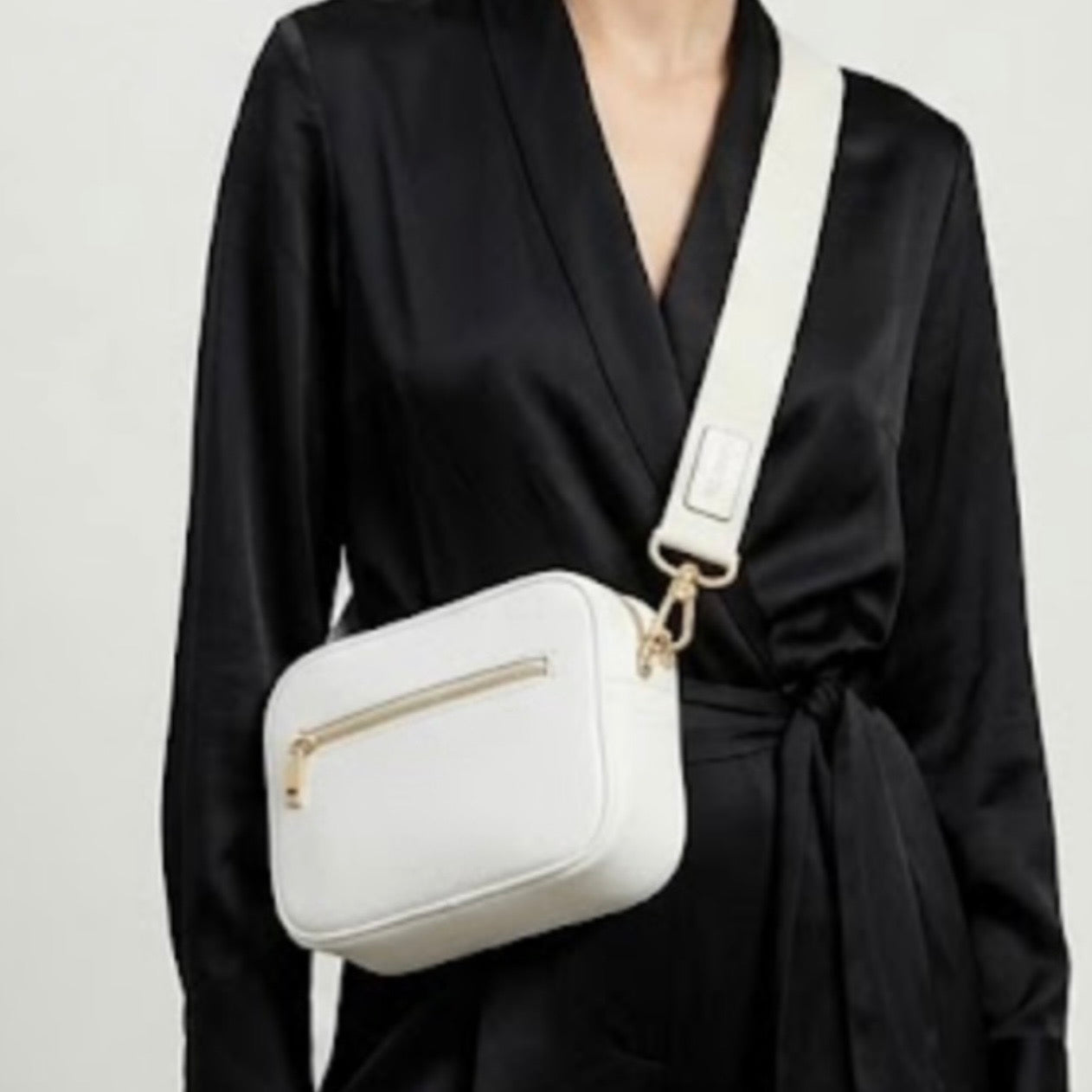 Classic pebbled leather cross body bag - White - TIKORI LONDON. Model in black silk cloths wear the crossbody. Front profile of the bag showing the zipper details and gold hardware in fully white background.