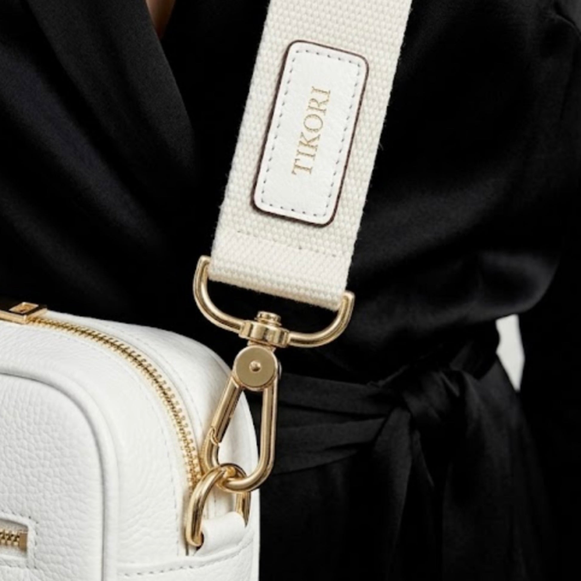 Classic elegance. Tikori Classic White by TIKORI london.  Genuine pebbled leather cross body bag. Model in black cloths wears the crossbody, close up detail of the golden hardware and TIKORI canvas strap shows in the picture. 