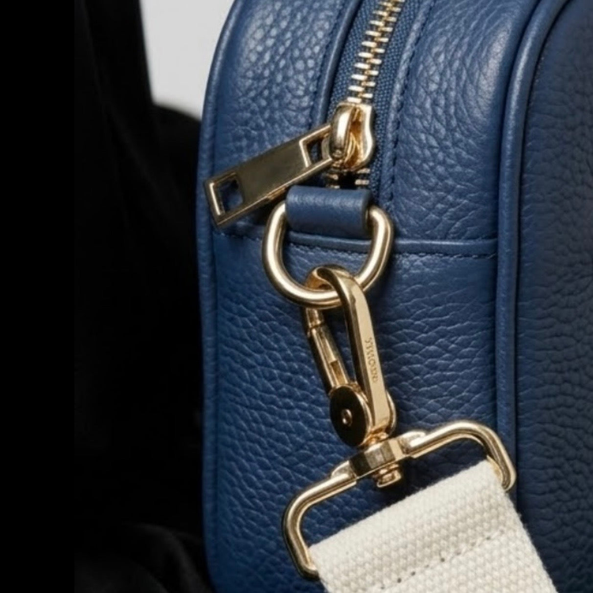 Classic elegance with practicality and versatility in mind. TIKORI classic Navy by TIKORI london. Genuine Leather cross body bag. Close up detail of the side profile of the bag showing with golden tone hardware and canvas strap. 