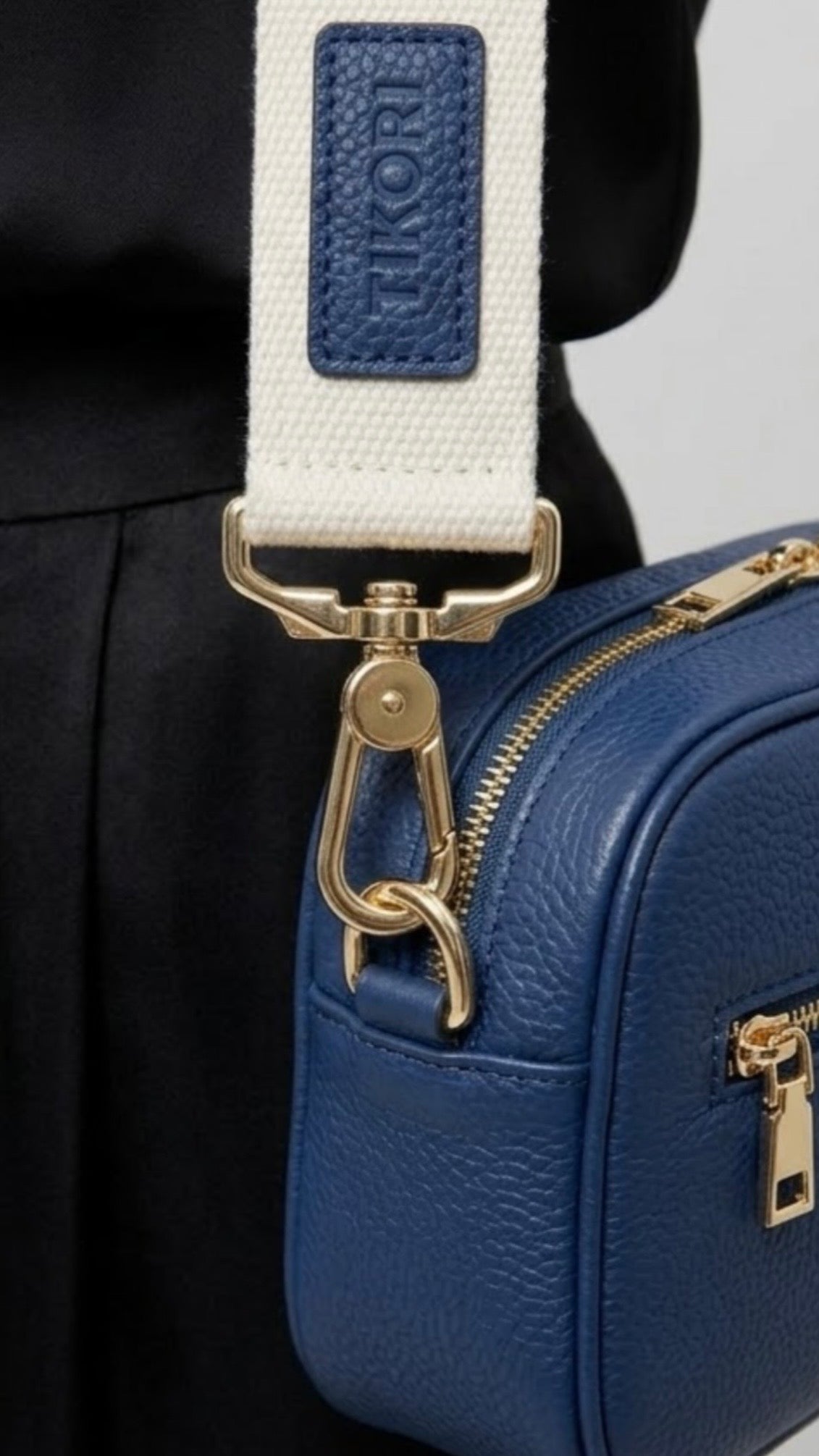 Classic elegance with practicality and versatility in mind. TIKORI classic Navy by TIKORI london. Genuine Leather cross body bag. Model in black silk cloths wears the crossbody. Close up detail of side profile of the bag showing with golden tone hardware and canvas strap.