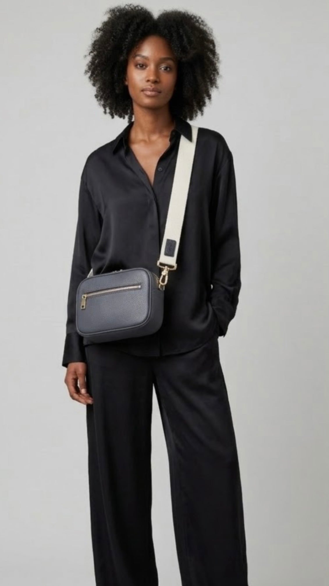 Classic elegance with practicality and versatility in mind. TIKORI classic grey purple by TIKORI London. Crossbody bag Crafted in soft pebbled premium genuine leather. Dark skinned beautiful Model in black silk cloths wears the crossbody. Front profile of the bag showing golden hardware and front pocket with zipper details in white background  