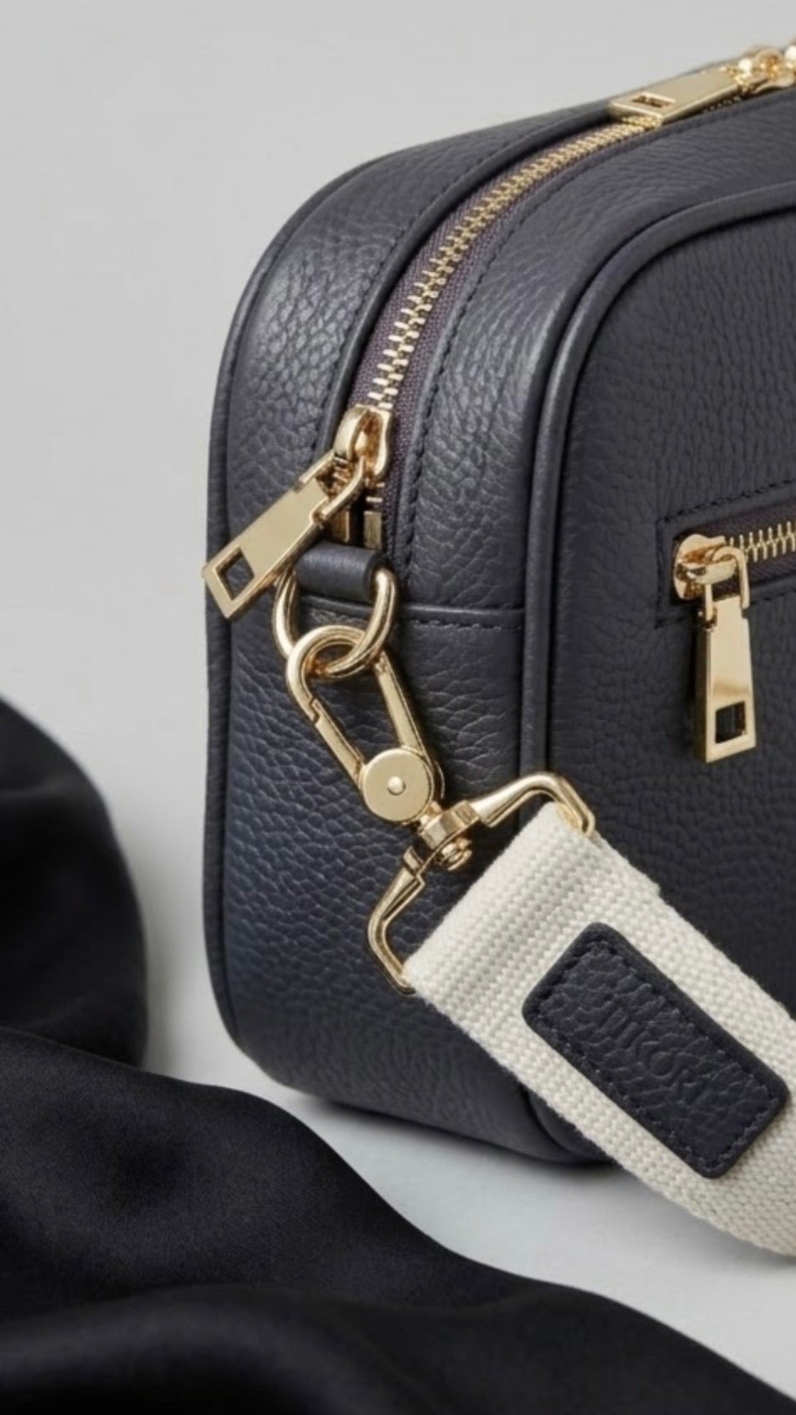 Classic elegance with practicality and versatility in mind. TIKORI classic grey purple by TIKORI London. Crossbody bag Crafted in soft pebbled premium genuine leather. Close up detail of the bags zipper and canvas strap shows in the picture 