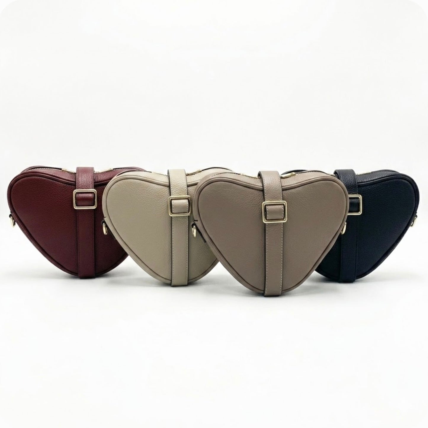 Selene heart-shaped leather crossbody bag by Tikori London with adjustable strap and gold-tone hardware. Front profile of all four bags showing in the picture facing front, the strap wrapped around the bag, showing the golden buckle. Soft off white background.