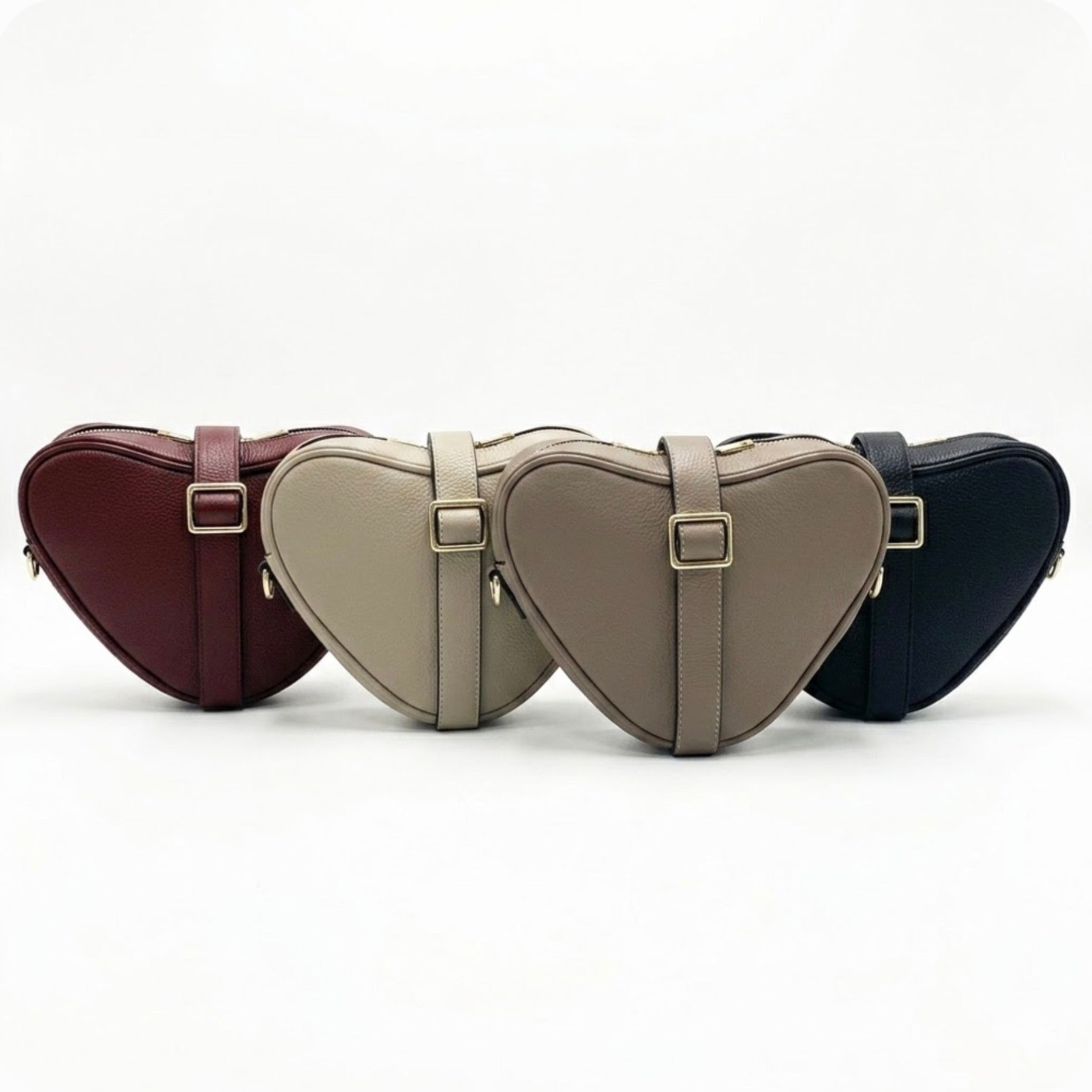 Selene heart-shaped leather crossbody bag by Tikori London with adjustable strap and gold-tone hardware. Front profile of all four bags showing in the picture facing front, the strap wrapped around the bag, showing the golden buckle. Soft off white background.