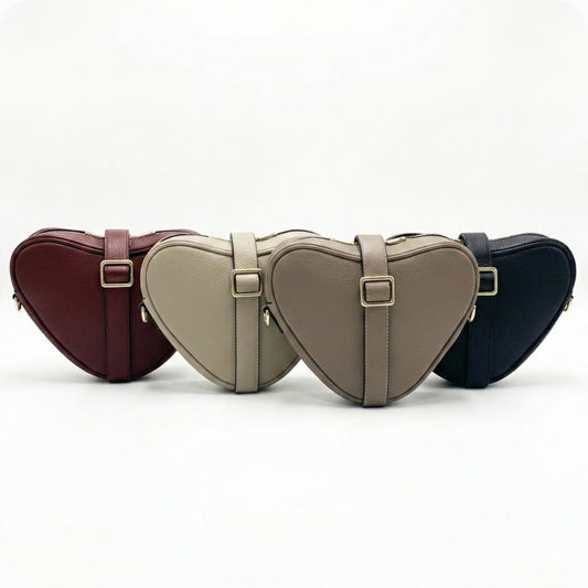 Selene heart-shaped leather crossbody bag by Tikori London with adjustable strap and gold-tone hardware. Front profile of all four bags showing in the picture facing front, the strap wrapped around the bag, showing the golden buckle. Soft off white background.