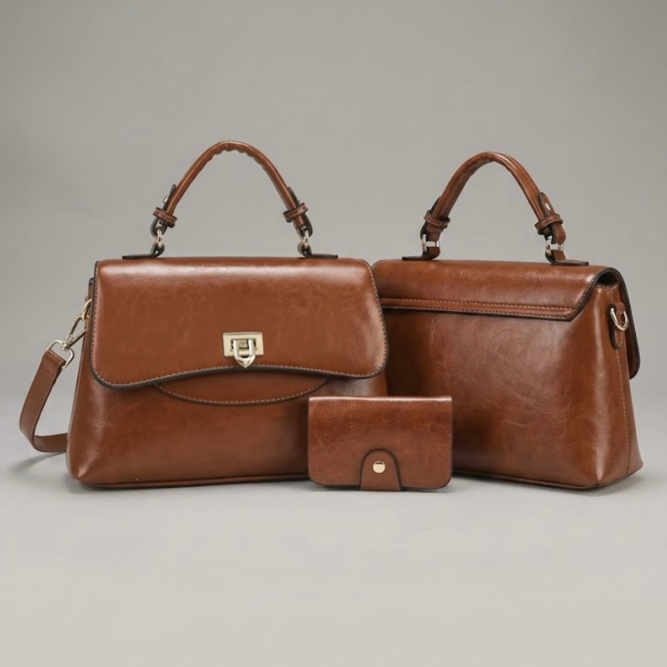 Heritage Flap Bag - Tan  By TIKORI London. Features a beautiful, sweeping front flap secured by a polished, shield shaped gold clasp. Top handle and long strap included. One bag facing front and another bag facing back showing the two profiles, next a small card holder. All three items display on the floor, 