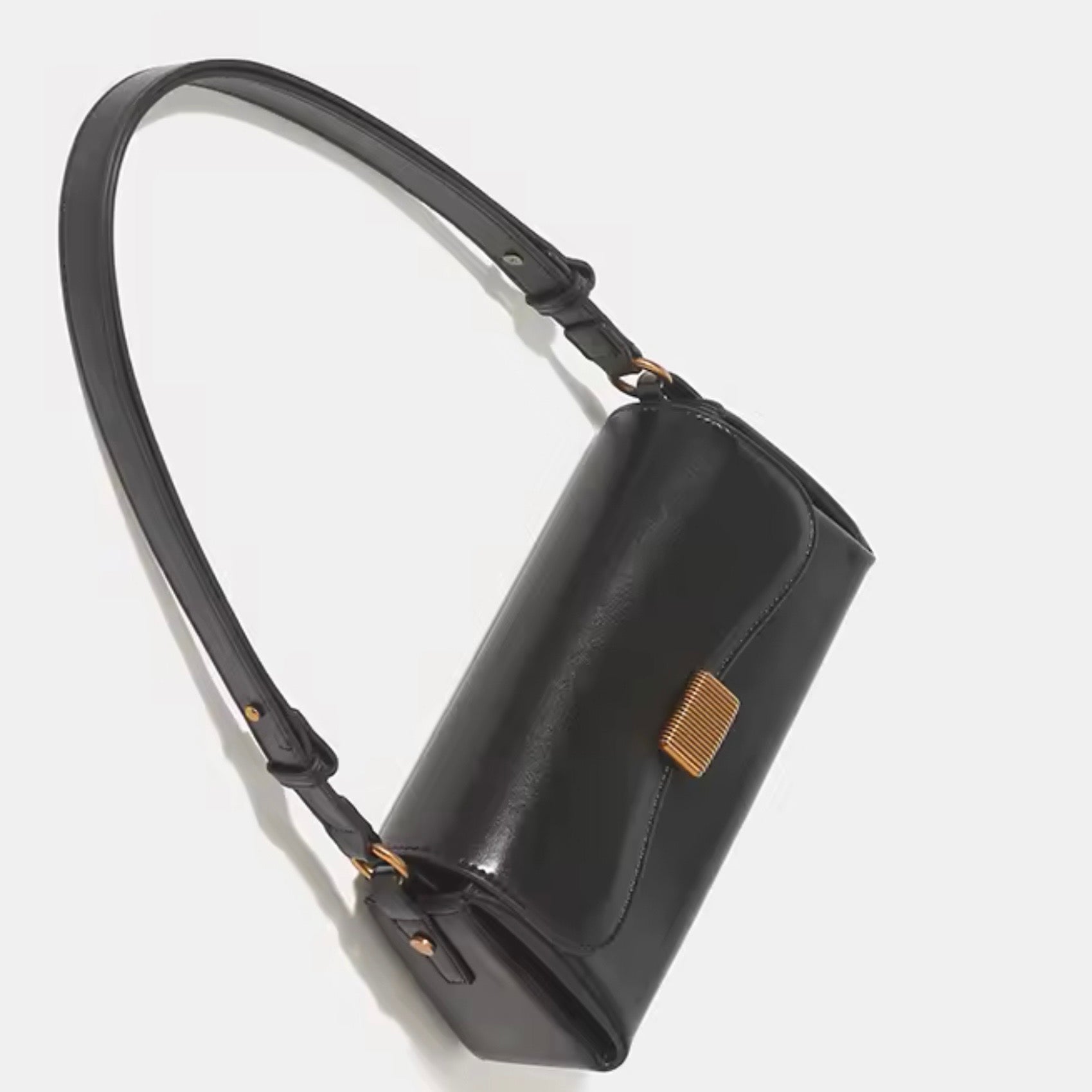 Crimson muse shoulder bag black by TIKORI London. Features a structured, elongated "baguette" body with clean, sharp lines and a narrow profile designed to sit snugly under the arm. Crafted in a vibrant, rich red, smooth polished premium high quality Vegan Leather. Black bag laid on the floor showing the front profile of the bag. Beautiful antique gold square closure showing in a fully white background.