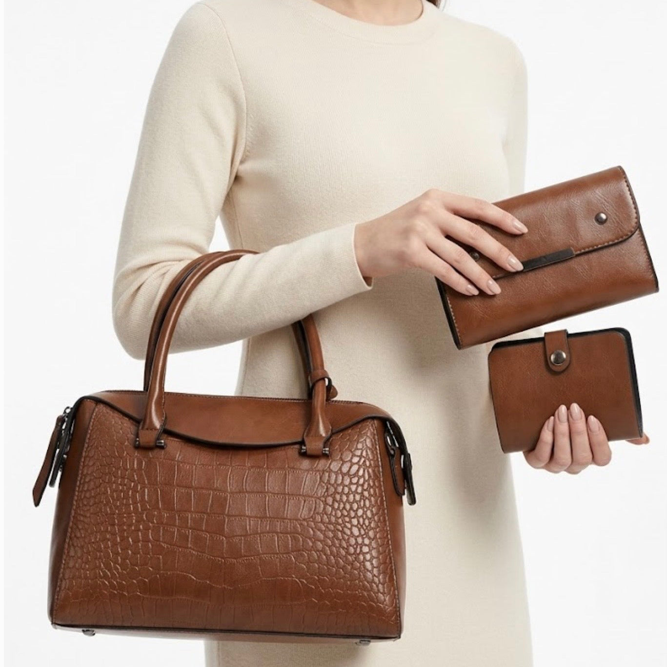 Vintage Inspired Embossed Satchel Bag tan by TIKORI LONDON. This elegant top handle handbag is crafted from rich, deep coffee toned high quality premium Vegan Leather, featuring a sophisticated crocodile embossed panel across the front for a multi textured look. Its structured "doctor bag" silhouette offers a spacious interior, secured by a smooth top zipper.  Beautiful model in ivory dress wearing the bag in her hand and she’s holding wallet and card holder in both hands. Cream background 