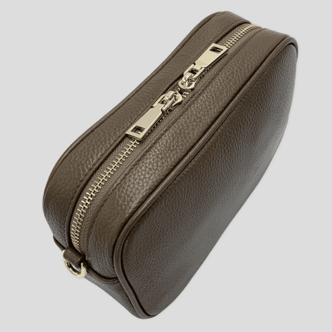 Tikori London classic pebbled leather crossbody bag in taupe with adjustable strap and silver hardware, resting on a neutral background.