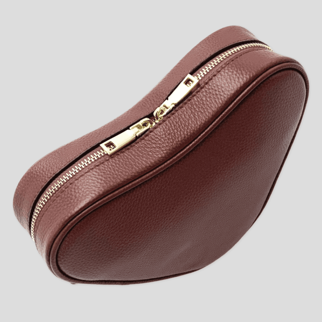 Red brown heart-shaped leather crossbody bag by Tikori London, showcasing its unique design and adjustable strap. Pictured from the top showing the zipper detail of the bag. Front profile of the bag in soft light grey background 